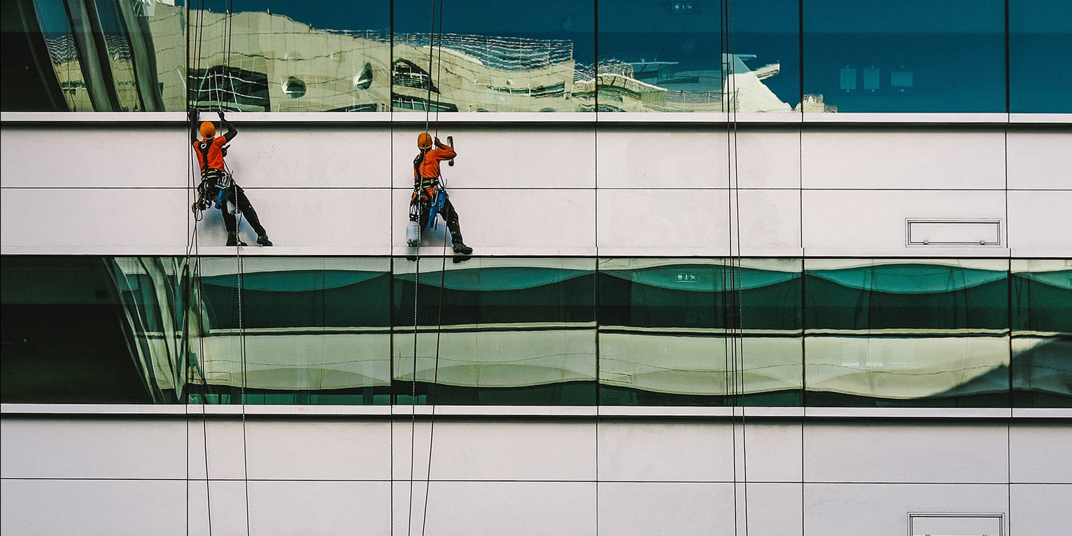 Window washers suspended on ropes cleaning the glass facade of a high rise